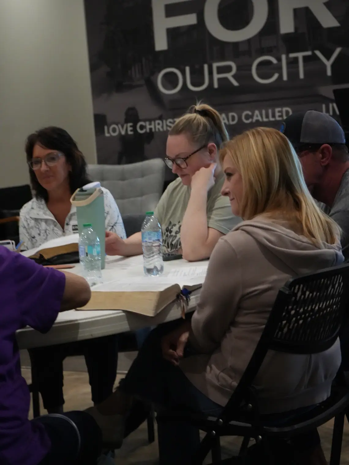 Adults around a table with open Bibles and study sheets, mid-conversation.