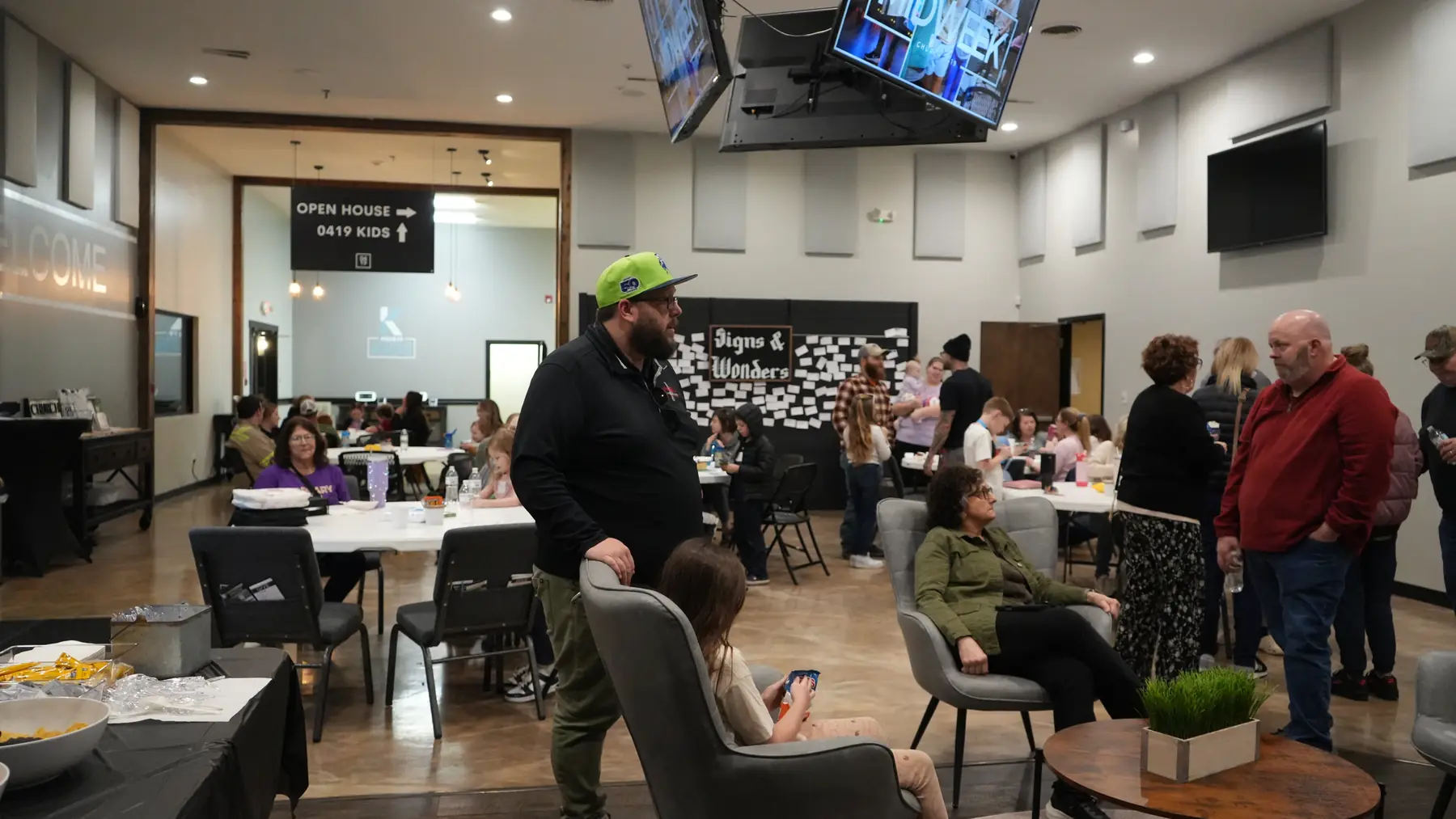 Families spread across the church hall before the night starts, kids at tables and adults standing and talking.